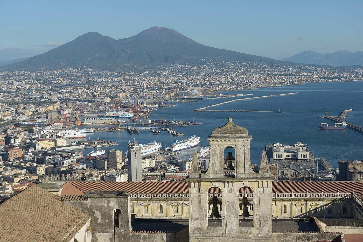 Il golfo di Napoli dall'alto: in primo piano il campanile della Certosa di San Martino, sotto la città e il porto con le navi, sullo sfondo il Vesuvio.